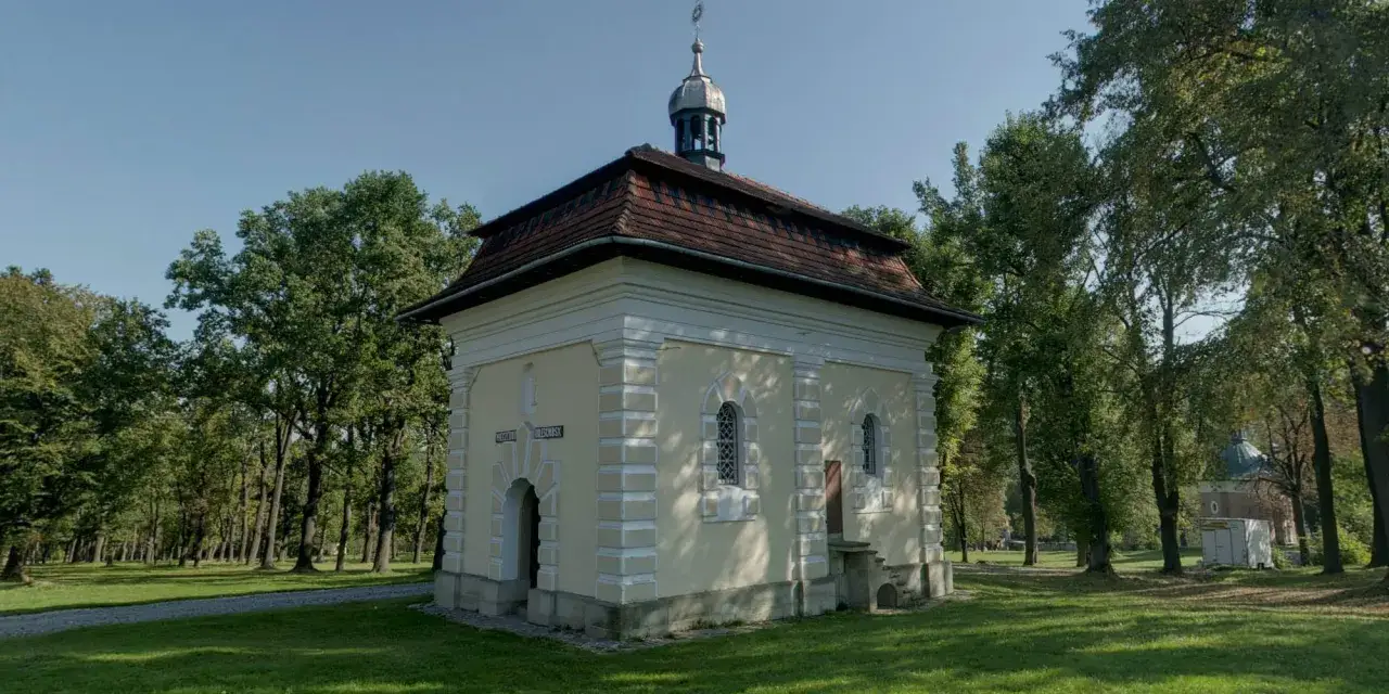 Kapliczka na Kalwarii Zebrzydowskiej, otoczona zielenią, z charakterystycznym dachem i wieżyczką.