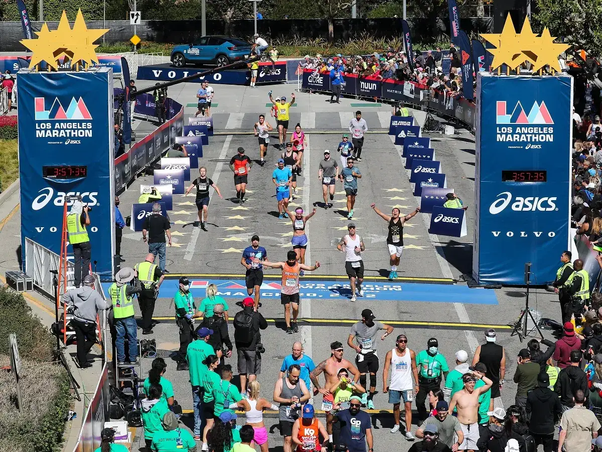 Uczestnicy maratonu w Los Angeles przekraczają linię mety. Czas na zegarze to 3:57:34. Długość maratonu to 42,195 km.