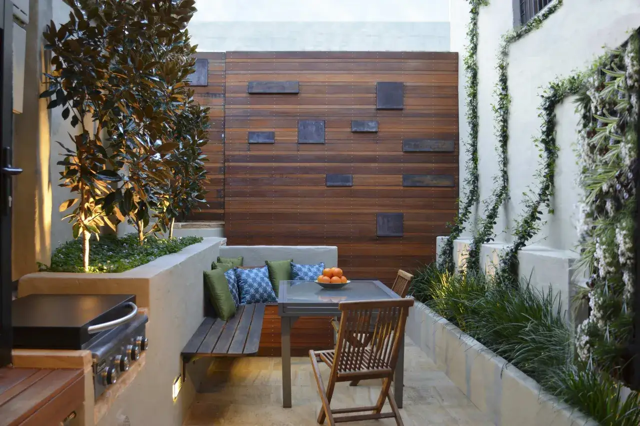 Un porche peque&ntilde;o con asientos de banco, mesa de cristal, sillas de madera, parrilla y vegetaci&oacute;n exuberante. Ideas para porches peque&ntilde;os.