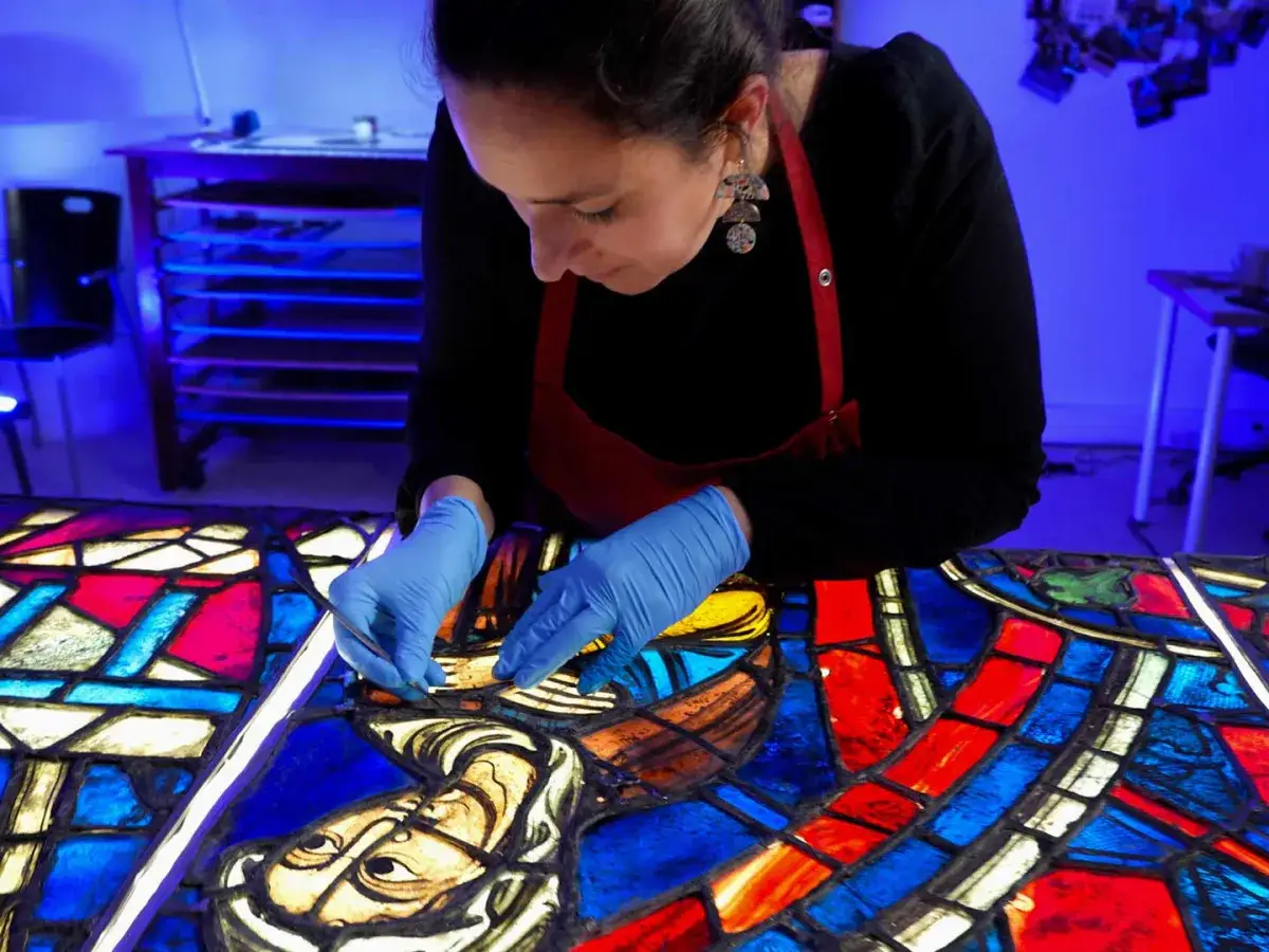 Artiste restauratrice travaillant avec soin sur des vitraux color&eacute;s, redonnant vie &agrave; des fragments d'histoire.