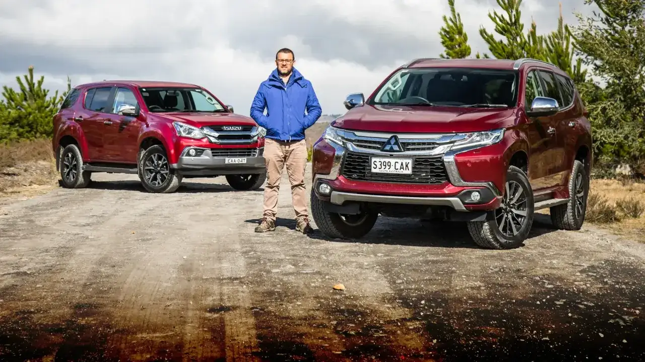 Mężczyzna stoi między dwoma czerwonymi SUV-ami. Po prawej stronie widać przód lśniącego Mitsubishi Pajero Sport, a po lewej Isuzu.
