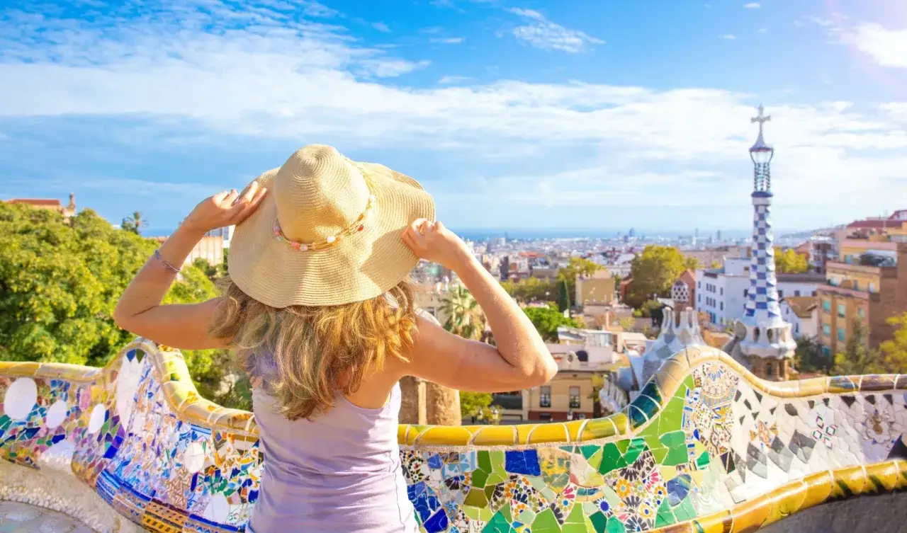 Kobieta w kapeluszu podziwia panoramę Barcelony z kolorowej ławki. Idealne miejsce na wakacje all inclusive.