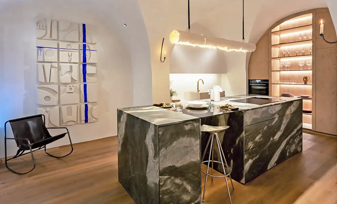 Elegante cocina con isla de mármol oscuro, arte abstracto en la pared y una silla de cuero.