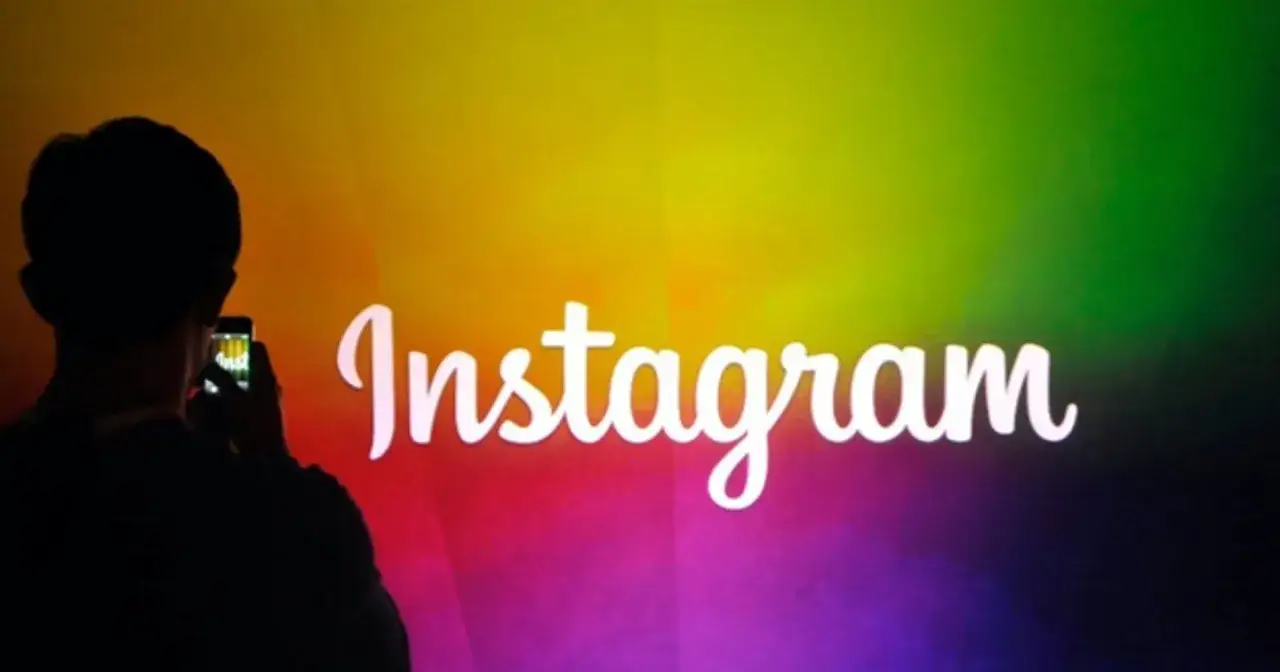 Osoba z telefonem na tle tęczowego logo Instagram. Wirtualny świat pełen jest zarówno piękna, jak i hejtu w internecie.