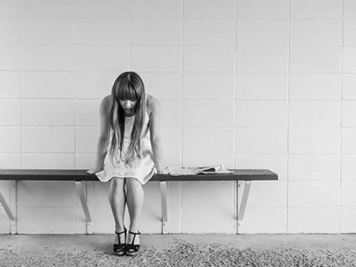 Mujer con vestido sentada en un banco, mirando hacia abajo, con expresi&oacute;n de sentirse culpable.