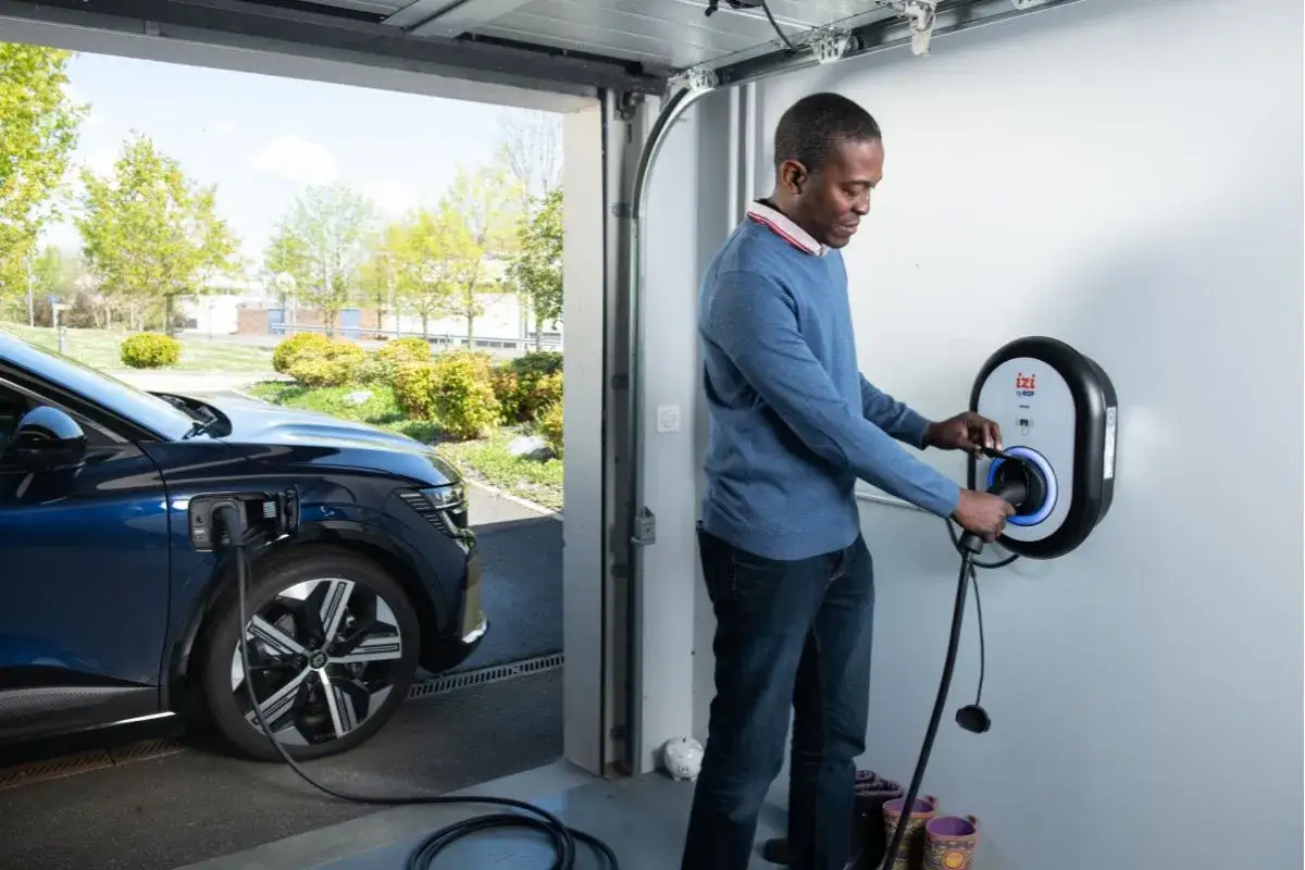 Un homme branche sa voiture électrique à une borne de recharge. Le contrôle technique du véhicule électrique est une étape importante pour sa longévité.
