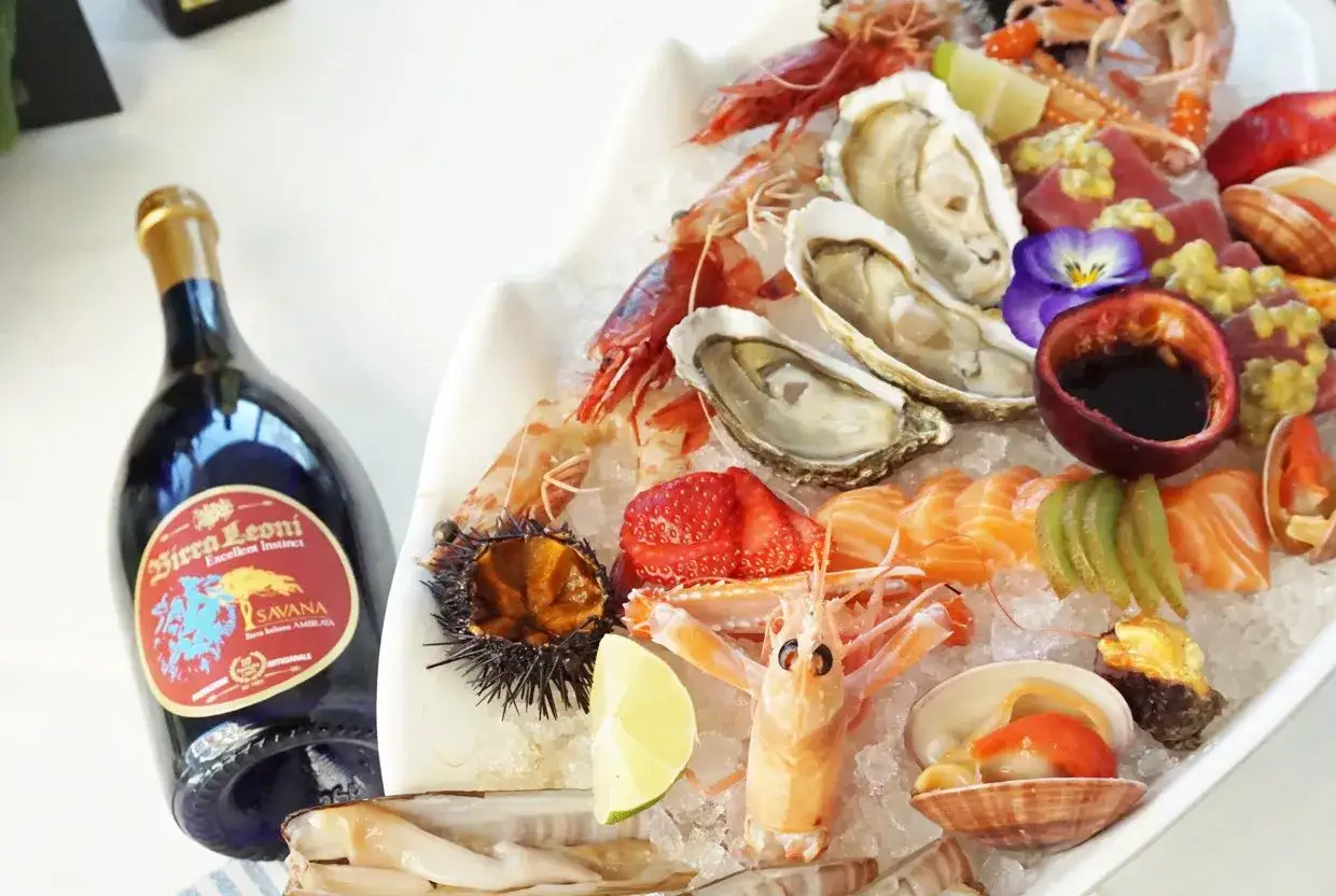 Un piatto di pesce crudo con ostriche, gamberi, salmone e tonno, accompagnato da una bottiglia di birra.