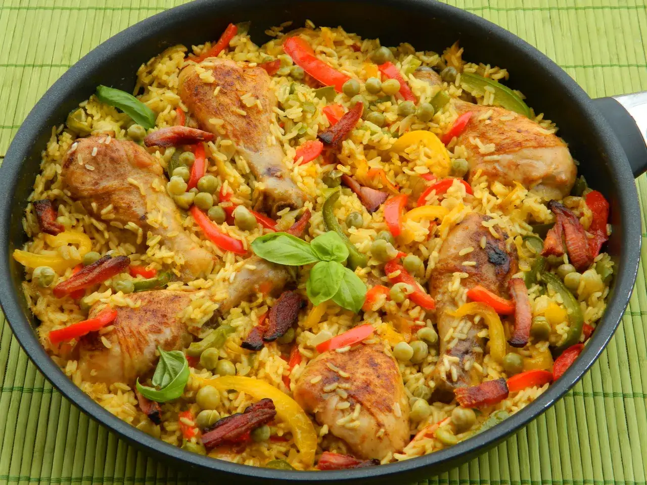 Pyszna paella z kurczakiem, ryżem, groszkiem, papryką i ziołami w czarnej patelni.