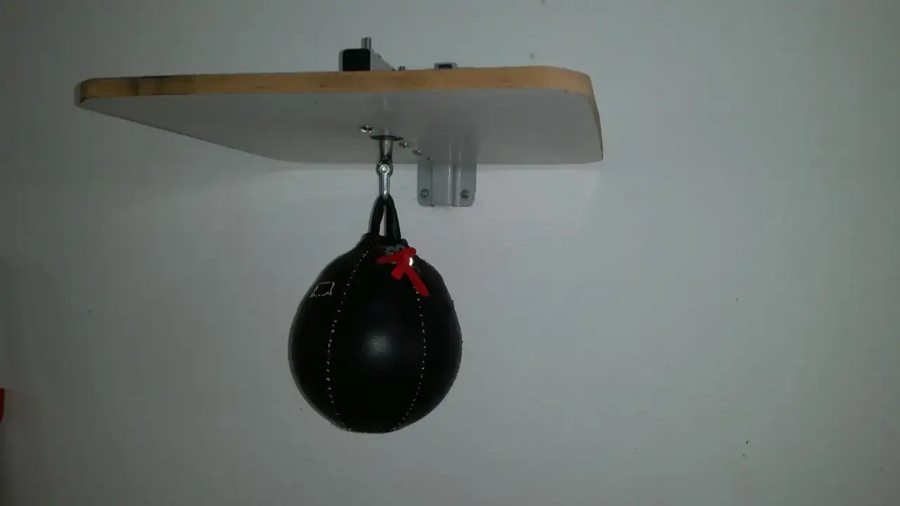 DIY speed bag setup: a black punching bag hangs from a wooden board mounted on a wall. This image shows how to make a speed bag station.
