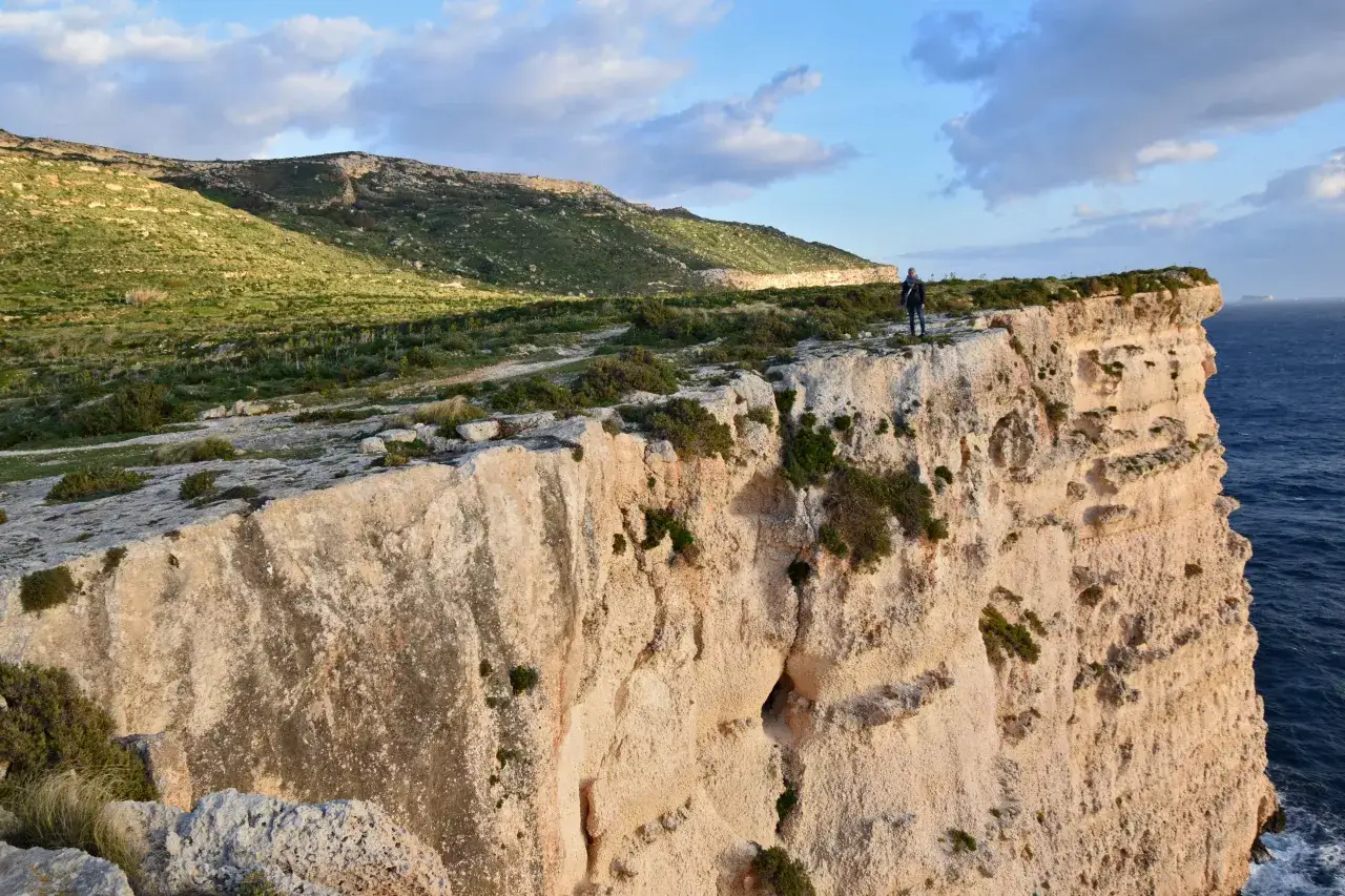 Osoba na klifie podziwia widok. To idealne miejsce na najciekawsze trasy spacerowe na Malcie i Gozo wzdłuż klifów.