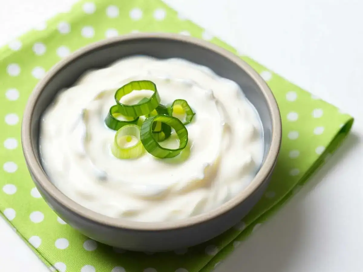 Cremiger Joghurt-Dip mit frischen Frühlingszwiebelringen garniert, serviert auf einem grünen Tupfentuch.