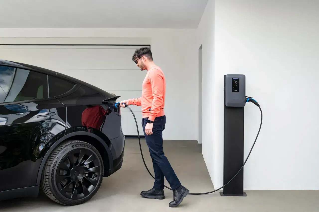 Uomo collega cavo di ricarica a auto elettrica nera. Stazione di ricarica visibile, indicando il futuro del consumo auto elettrica.