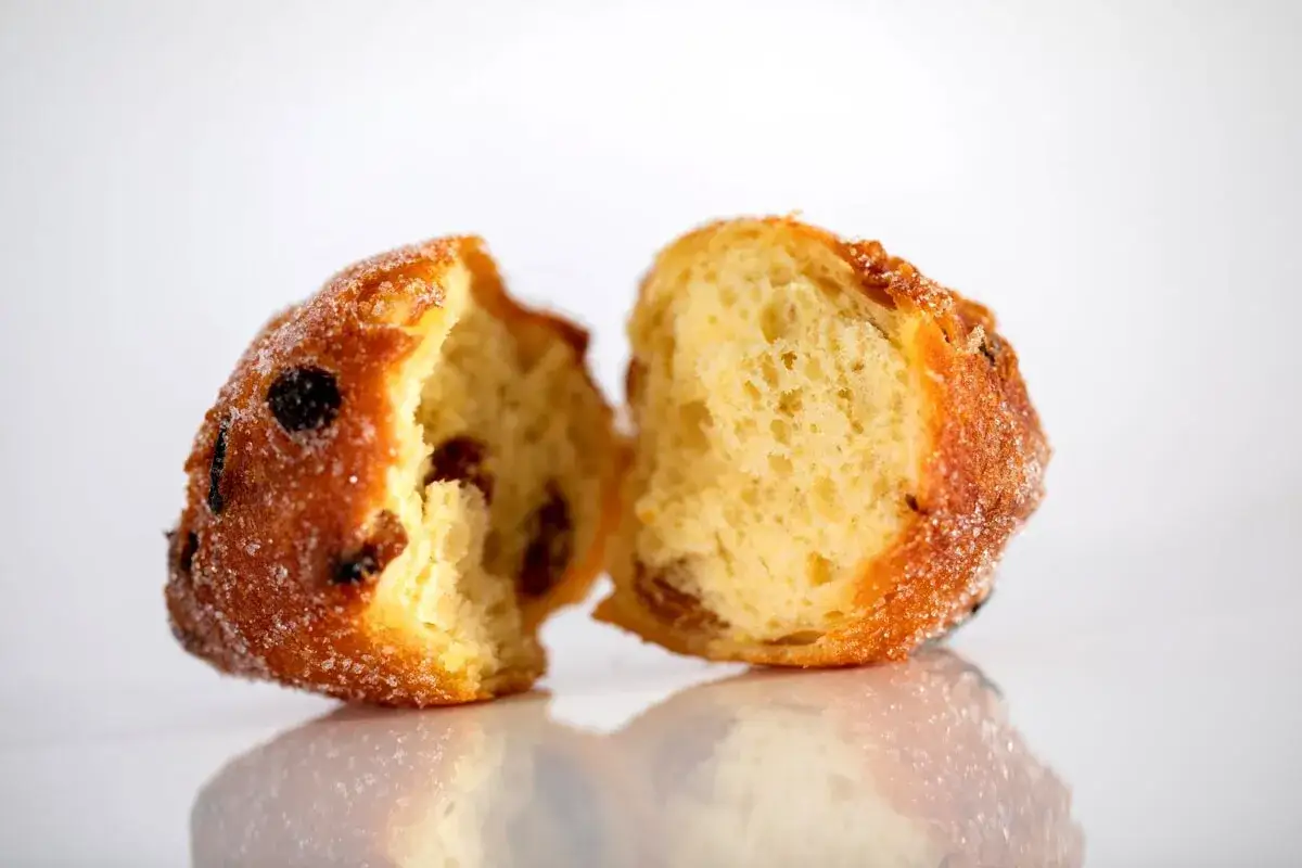 Frittelle veneziane, dolci e soffici, con uvetta e zucchero, spezzate a metà per mostrare l'interno invitante.