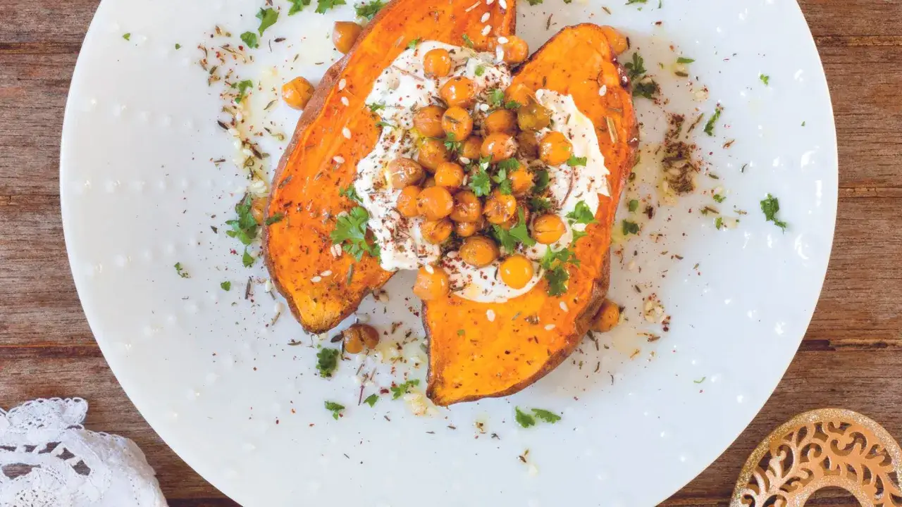 Deux moitiés de patate douce rôties, garnies de pois chiches, de crème et de persil, sur une assiette blanche.