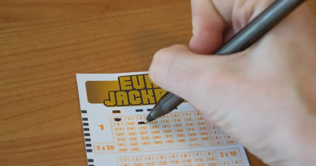 Ręka zaznacza liczby na kuponie Eurojackpot. Czy zwycięzcy dostają specjalne karty płatnicze bez limitów?