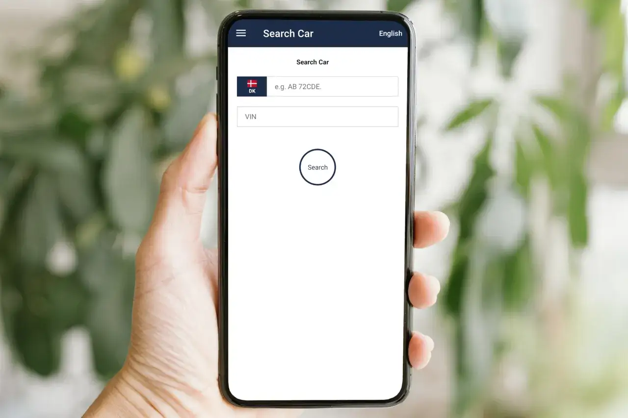 En hand h&aring;ller en mobil med en app f&ouml;r att s&ouml;ka bil. F&auml;lt f&ouml;r registreringsnummer och VIN-nummer finns, med en knapp f&ouml;r att s&ouml;ka.