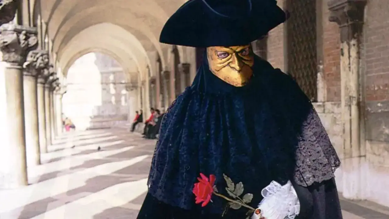 Un personaggio mascherato, forse un Casanova a Venezia, con maschera dorata e rosa rossa, passeggia sotto un portico.
