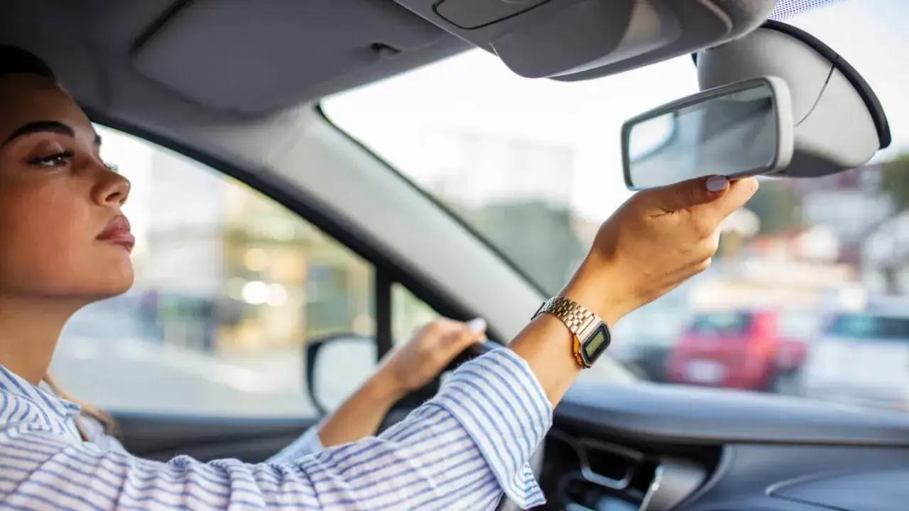 Mujer ajustando el retrovisor interior del coche. Siempre hay que mirar por los retrovisores para conducir segura.