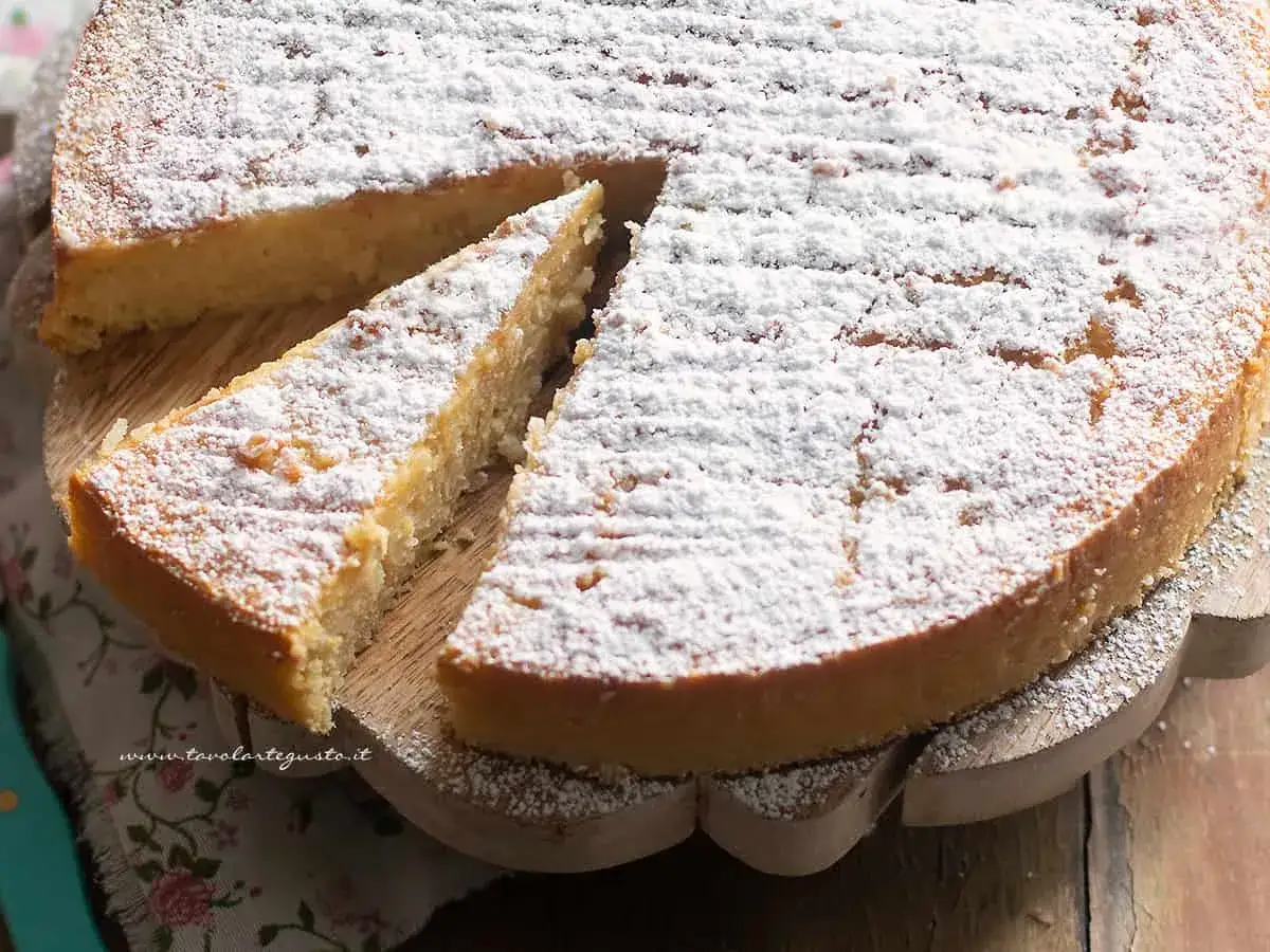 Una fetta di torta di riso, soffice e profumata, cosparsa di zucchero a velo. La torta di riso ricetta della nonna, un classico intramontabile.