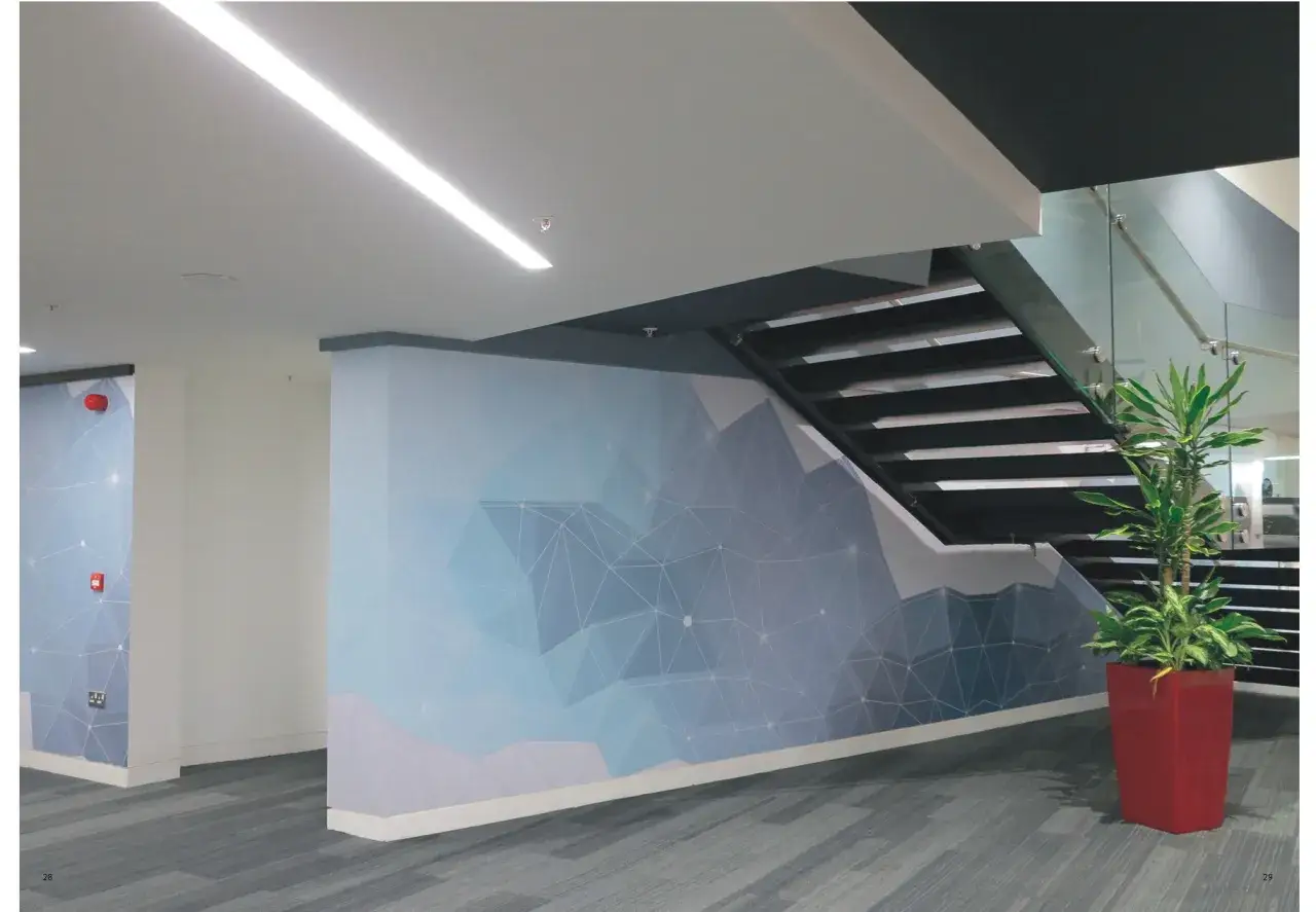Modern oficina con escaleras y murales de diferentes tipos de vinilos con diseño geométrico azul. Planta en maceta roja.