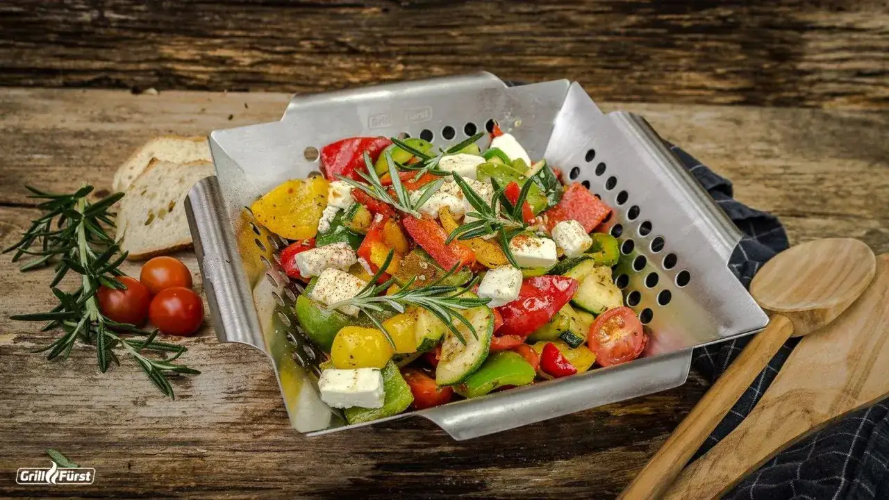 Buntes, vegetarisches Grillgut mit Paprika, Zucchini, Tomaten und Feta in einer Grillpfanne, garniert mit Rosmarin.