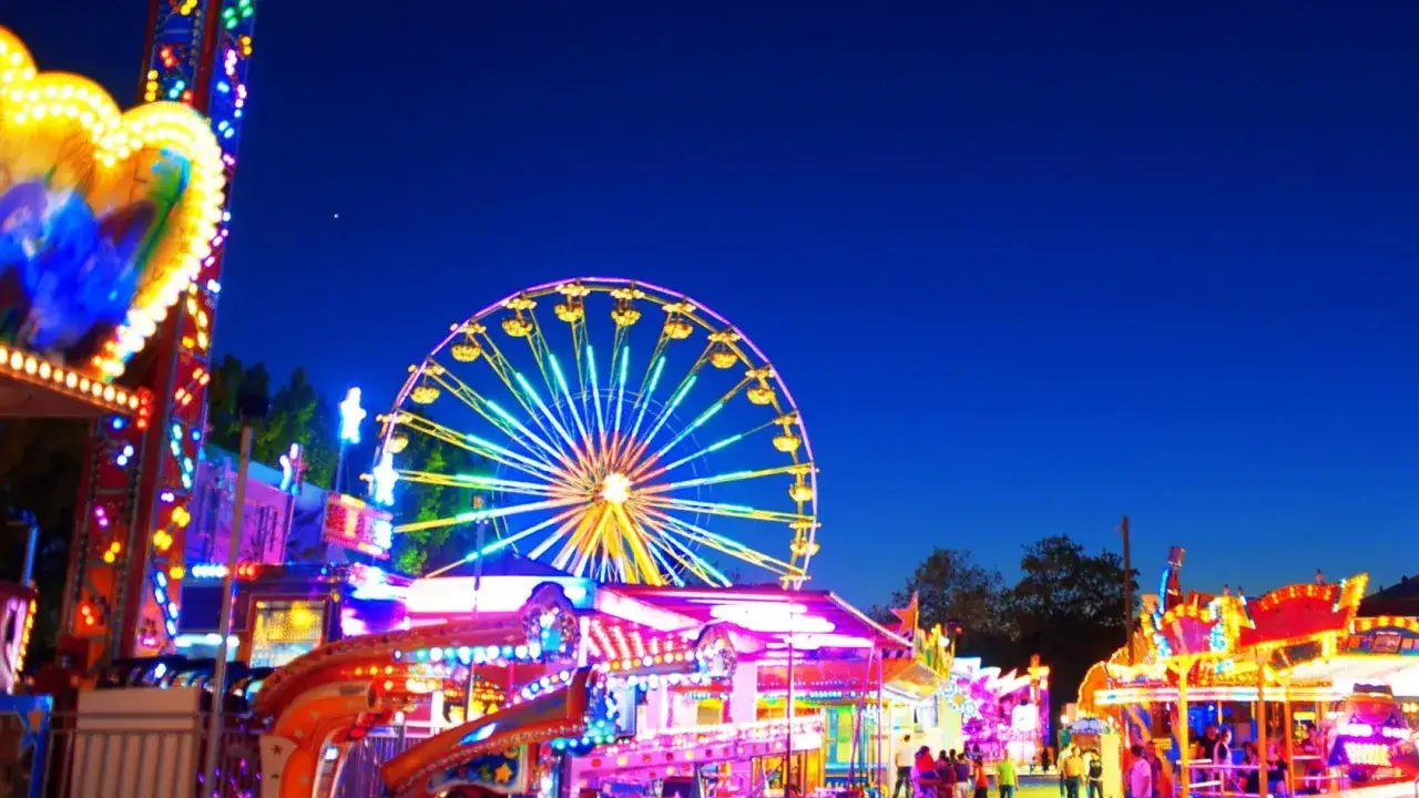 Luna park illuminato di notte, con ruota panoramica e giostrai sinti che animano la festa.