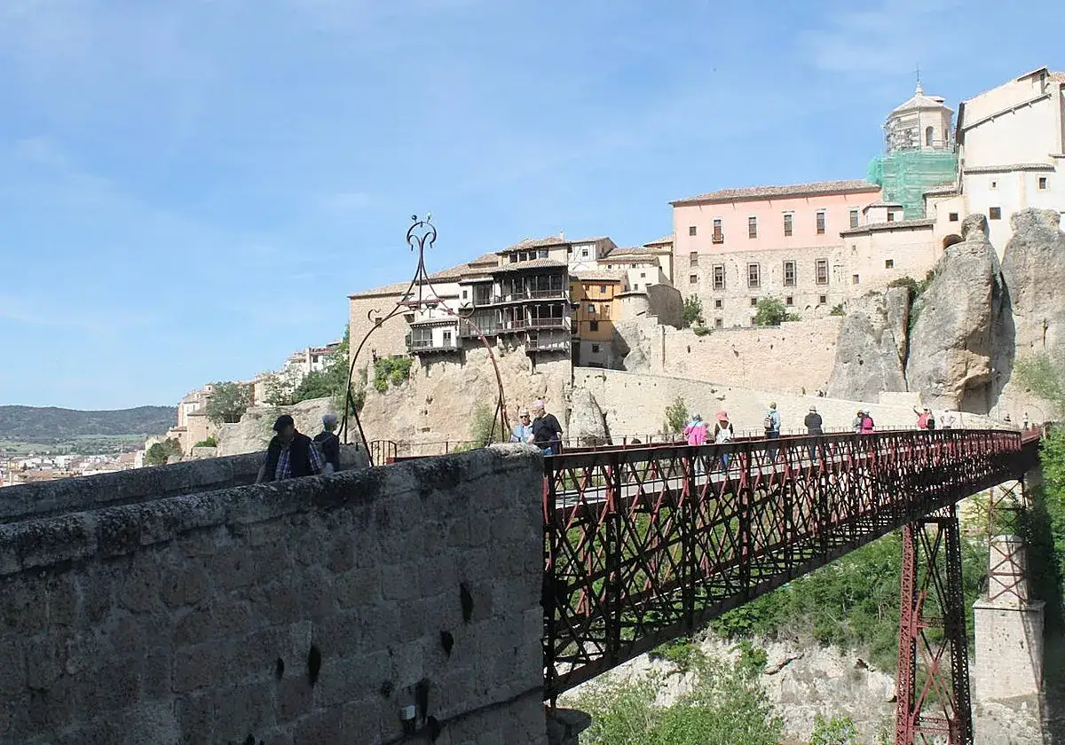 Gente pasea por el puente de San Pablo en Cuenca, con las casas colgadas al fondo.
