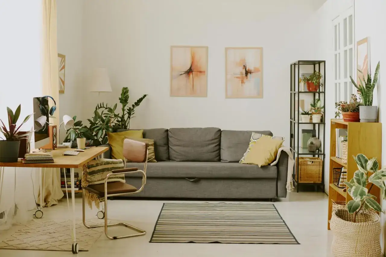 Przytulny salon z biophilic design: kanapa, biurko, rośliny i obrazy tworzą harmonijną przestrzeń.