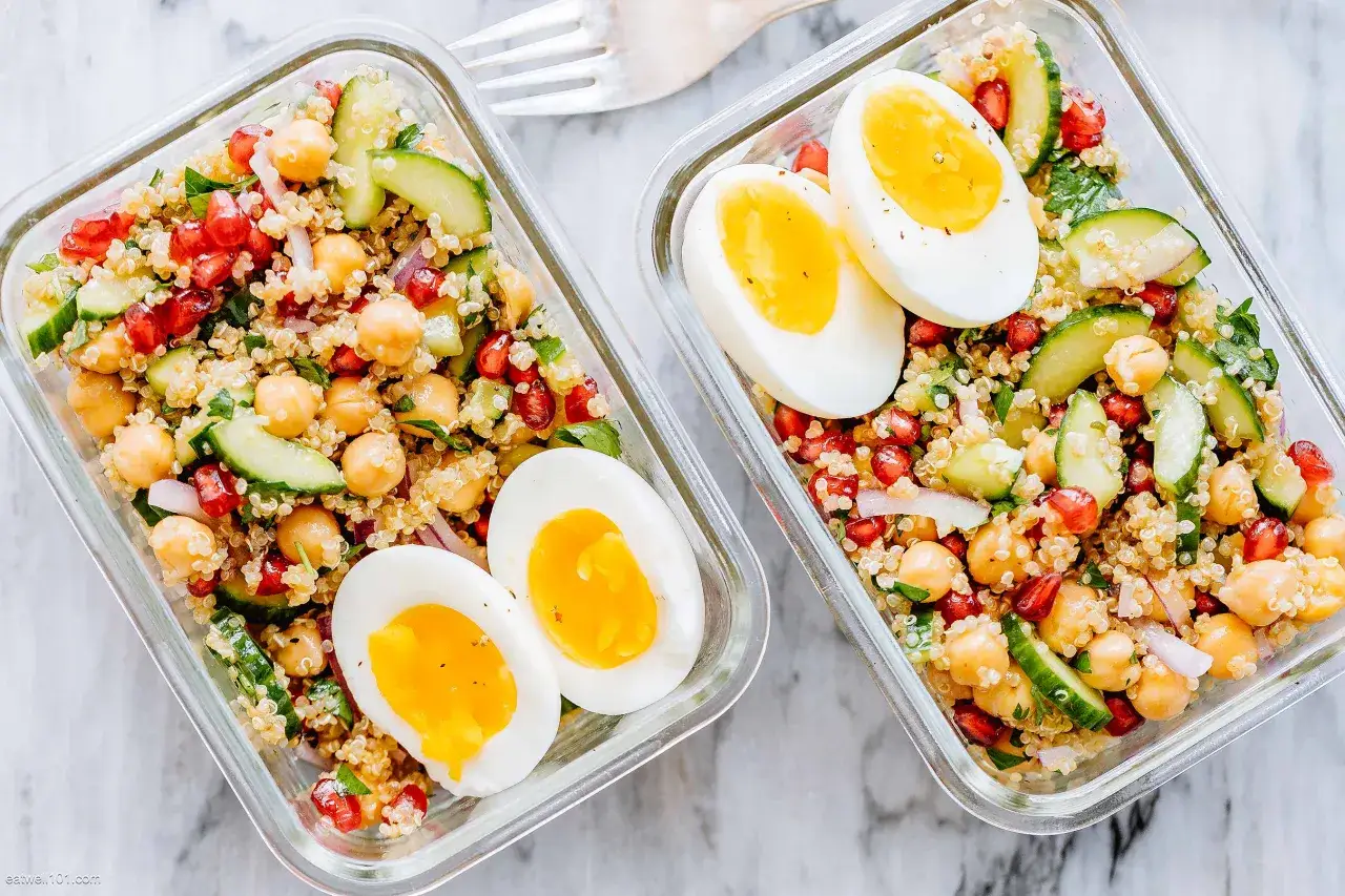 Zwei Behälter mit Quinoa Salat, Kichererbsen, Granatapfel, Gurke und gekochten Eiern.