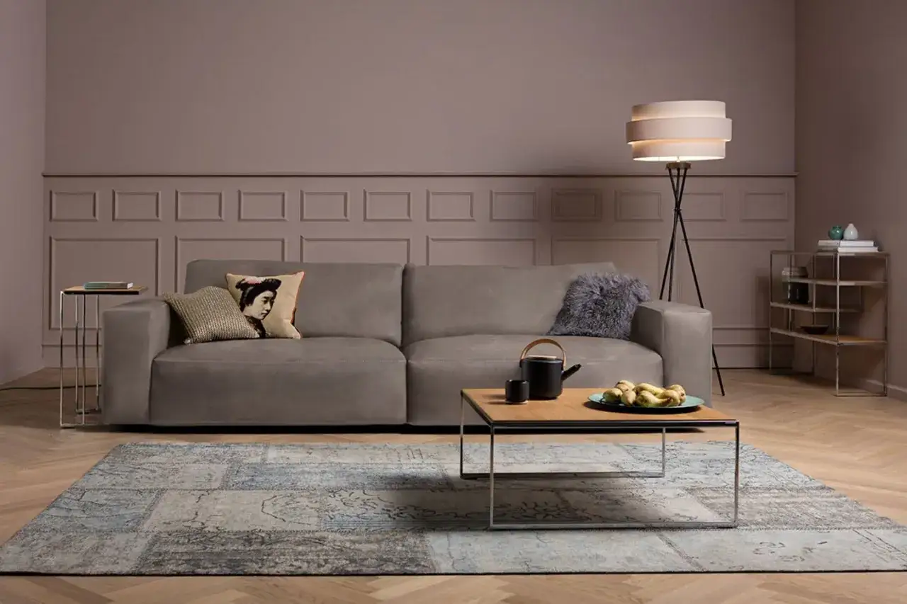 Gemütliches Wohnzimmer mit einem Sofa in der Farbe Taupe, einem Couchtisch mit Teekanne und Früchten, einem Teppich und einem Stehlampen.