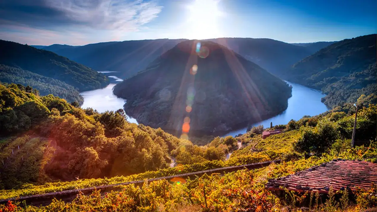Un río serpentea entre colinas verdes, creando una curva espectacular que parece el **cabo do mundo**. El sol brilla intensamente, iluminando el paisaje.