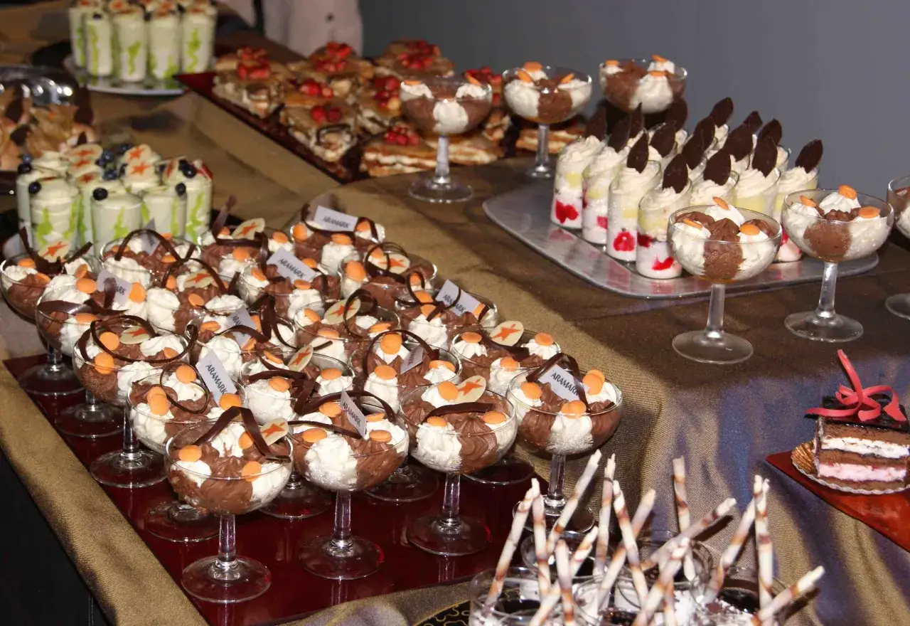 Una mesa llena de deliciosos postres caseros, incluyendo copas de mousse de chocolate y crema, y pasteles decorados.