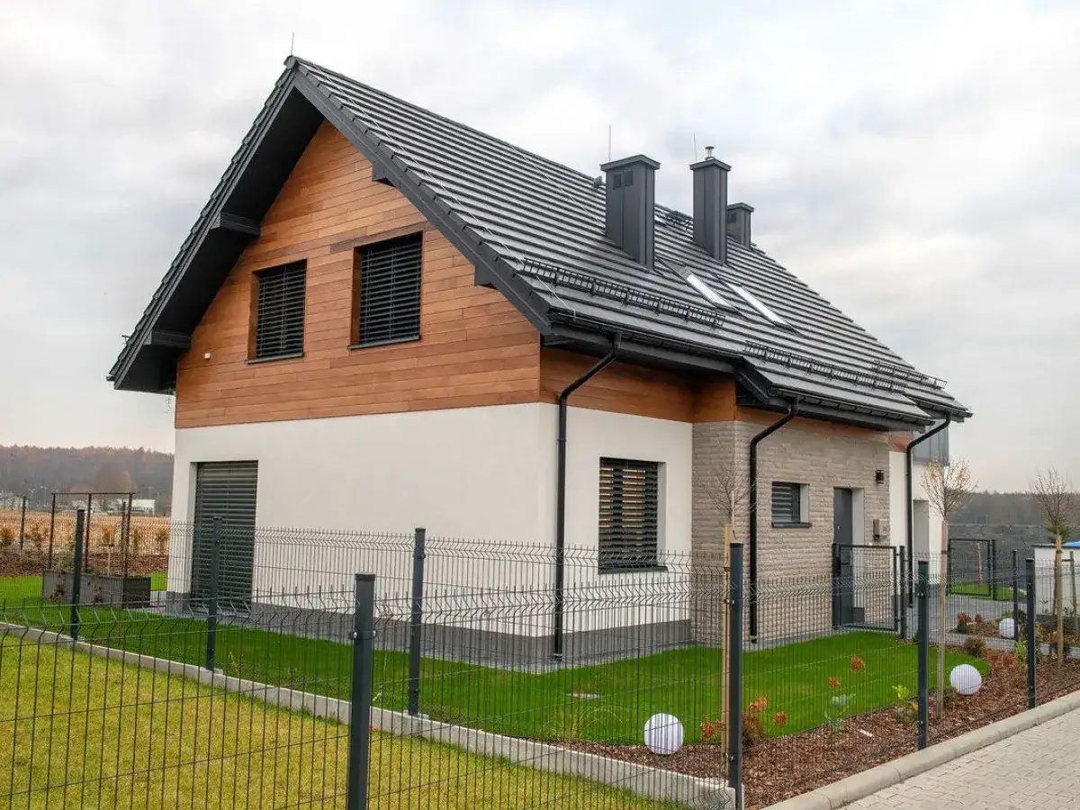 Nowoczesny dom z drewnianą elewacją i ciemnym, **dachem dwuspadowym**. Ogrodzony zadbanym trawnikiem.