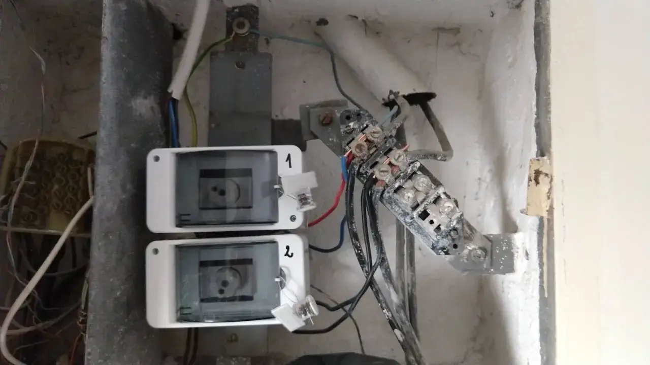 Dwa liczniki energii elektrycznej, oznaczone 1 i 2, podłączone do starej, zakurzonej instalacji. Widać luźne przewody i złącza, typowe dla starszych budynków. tn-c.