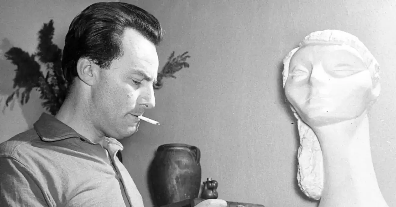 Andrzej Munk, twórca filmów, z papierosem w ustach, obok rzeźby.