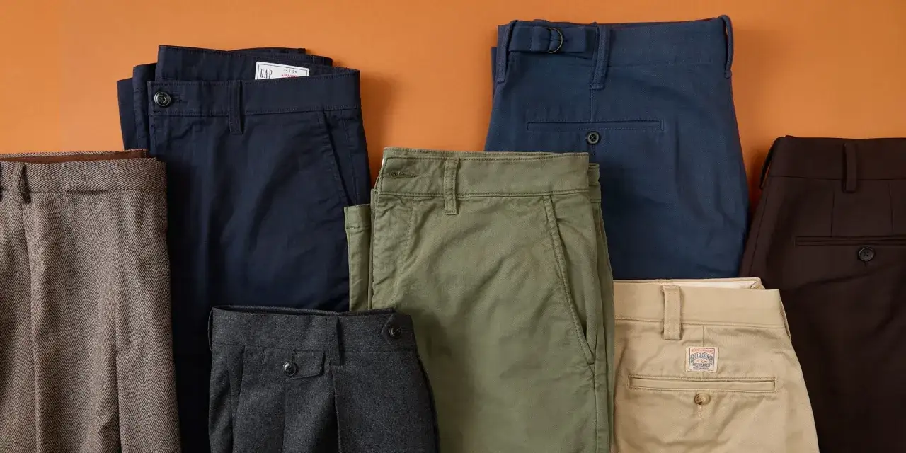 A collection of neatly folded chinos in various colors like navy, olive green, khaki, and brown. These are not sweatpants, but rather smart casual trousers.