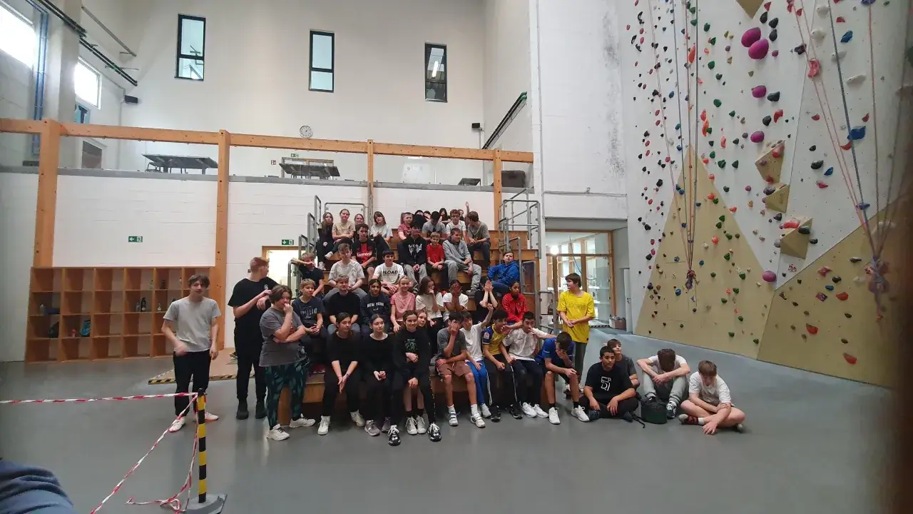 Eine Gruppe Jugendlicher sitzt in einer 2t Kletterhalle, bereit f&uuml;r den Kletterspa&szlig;.