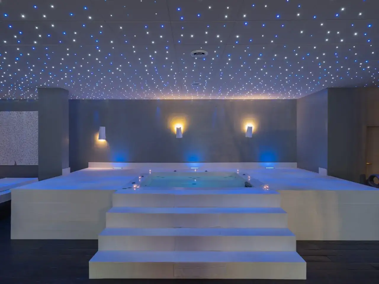 Un espace détente avec un bassin d'eau illuminé par des lumières bleues et un plafond étoilé. Ce **chromothérapie spa** invite à la relaxation.