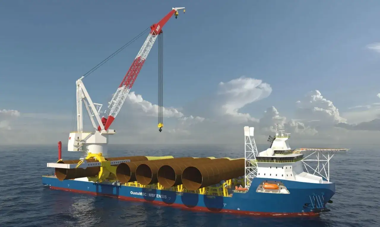 Bateau grue transportant des éléments de fondation pour une éolienne en mer. Le navire est équipé d'une grue imposante et de plusieurs tubes cylindriques.