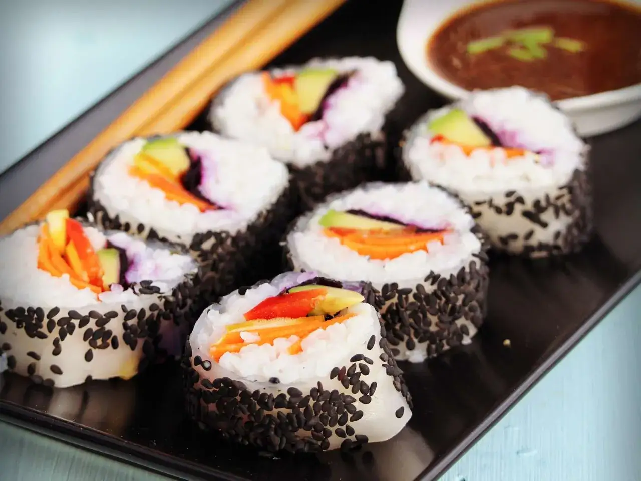 Veganes Sushi mit bunter Füllung aus Avocado, Karotte und Paprika, umhüllt von schwarzen Sesamkörnern. Köstliche vegane Sushi Füllung!