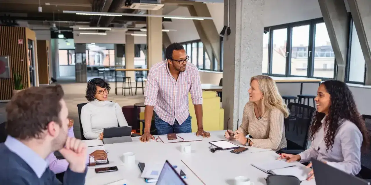 A diverse team collaborates around a table. The board chair, a man in a plaid shirt, leads the discussion, embodying what a board chair does: guiding strategy and fostering teamwork.
