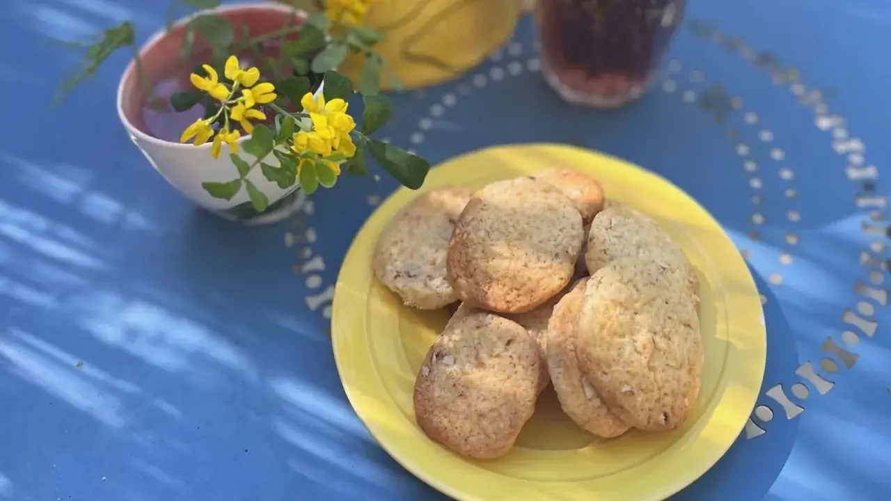 Gyllene bondkakor på en gul tallrik, perfekta att baka med detta recept. En kopp te och gula blommor fulländar bilden.