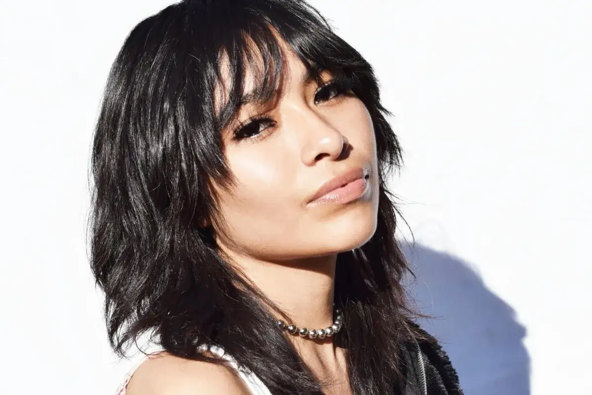 Mujer con un moderno corte de pelo mullet, labios brillantes y un collar de cuentas plateadas.