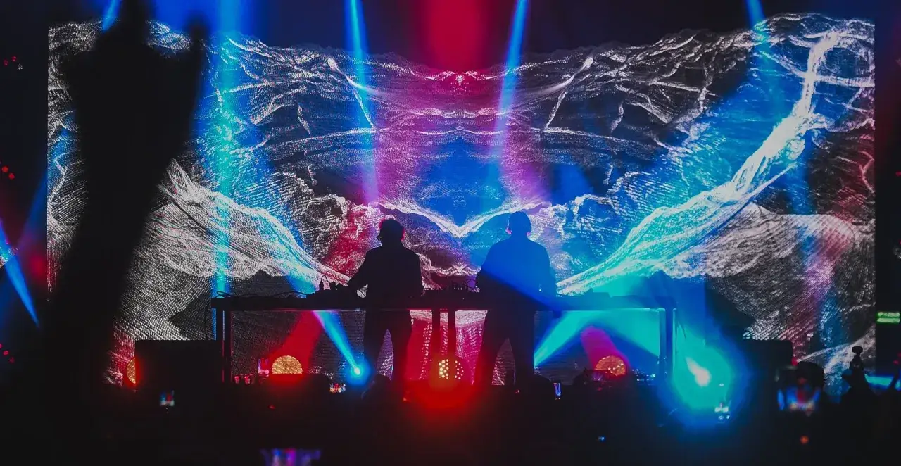 Dwóch DJ-ów na scenie Tauron Nowa Muzyka, w tle wizualizacje w kolorach niebieskim i różowym.