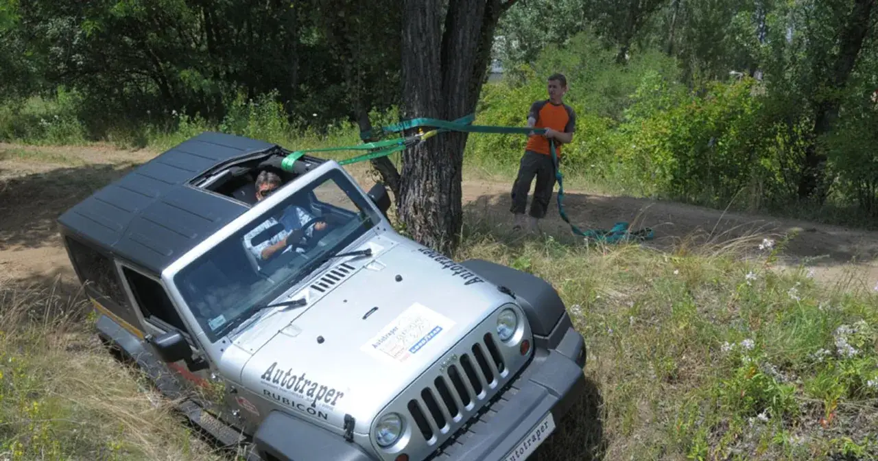Srebrny Jeep Rubicon z otwartym dachem, używany do pokonania zbocza g&oacute;ry w poprzek, z liną zaczepioną o drzewo.