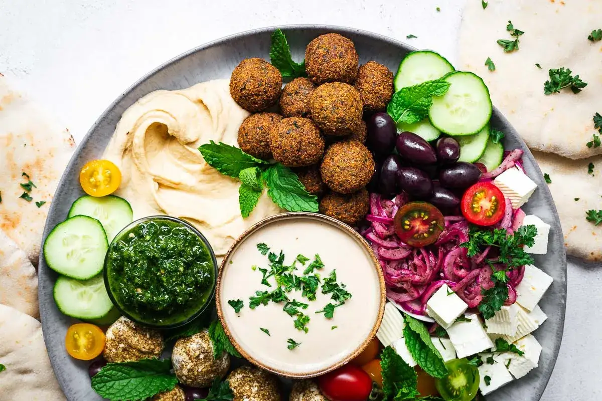 Talerz pełen smakołyków: co to jest falafel? Chrupiące kulki, hummus, oliwki, ser feta, warzywa i sos tahini. Idealna przekąska.