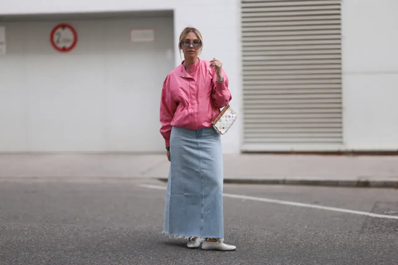 Kobieta w różowej kurtce i długiej jeansowej spódnicy prezentuje modne stylizacje z jeansową spódnicą.