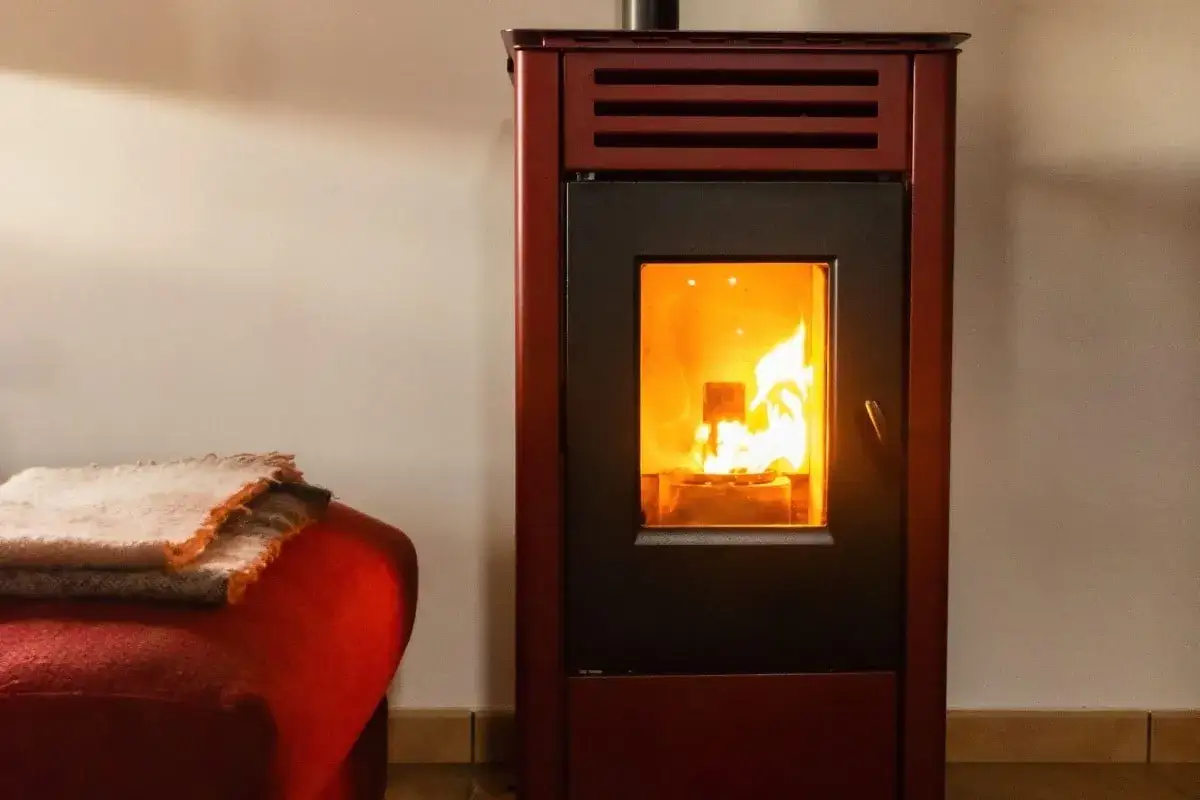 Poêle à granulés rouge, flammes vives visibles. Confort et chaleur pour une consommation maîtrisée. Couvertures douces sur un fauteuil à proximité.