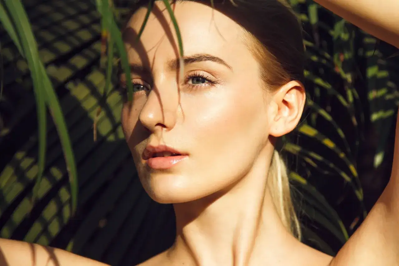 Kobieta z promienną, dewy skin, otoczona liśćmi palm.