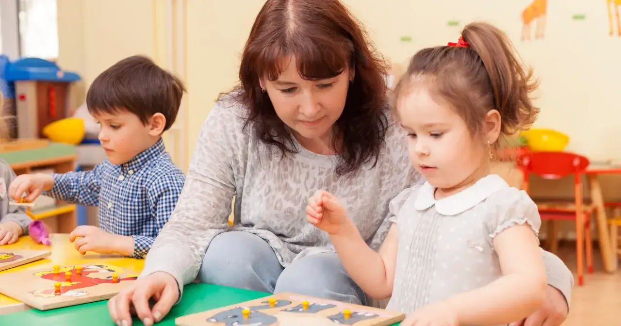 Nauczycielka wspiera wczesne wspomaganie rozwoju dzieci, pomagając im układać puzzle.